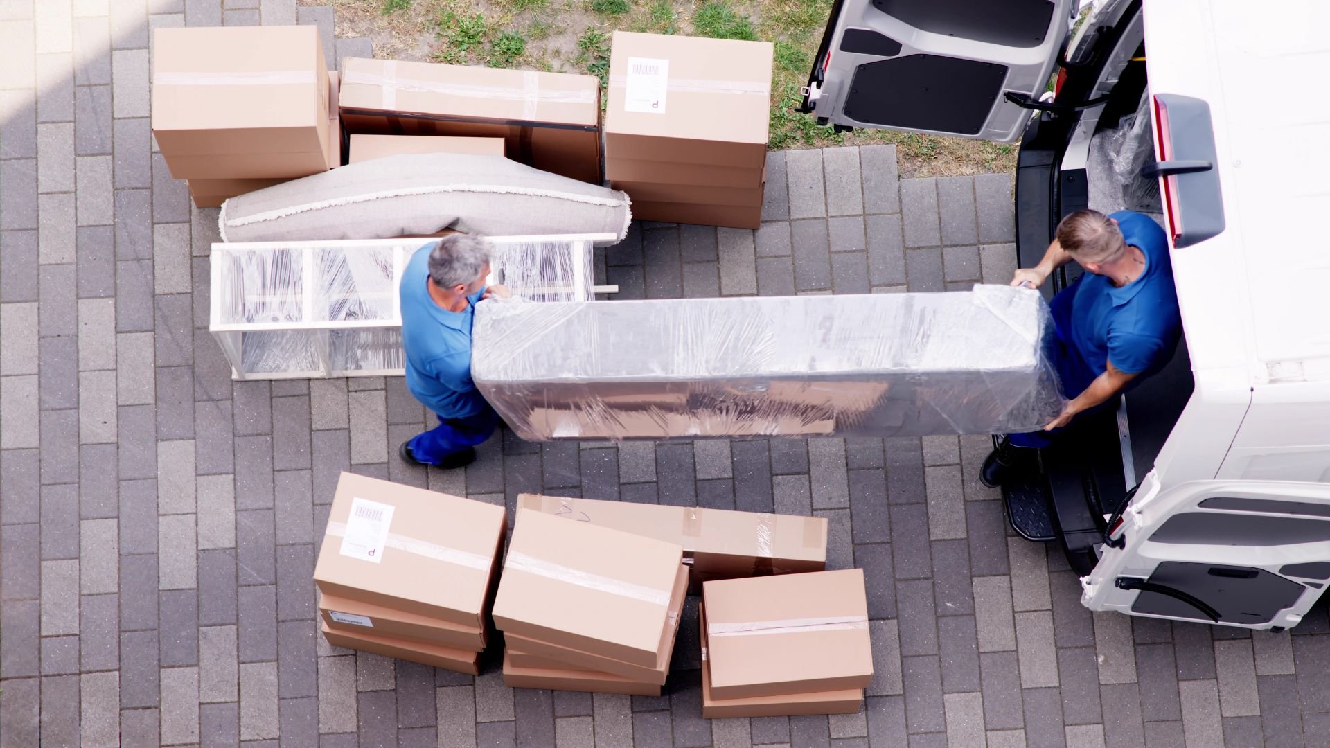 Movers carrying wrapped furniture and boxes next to moving truck