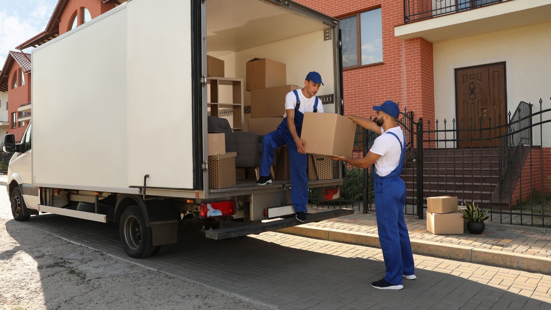 Movers loading cardboard boxes into a white delivery truck near a house