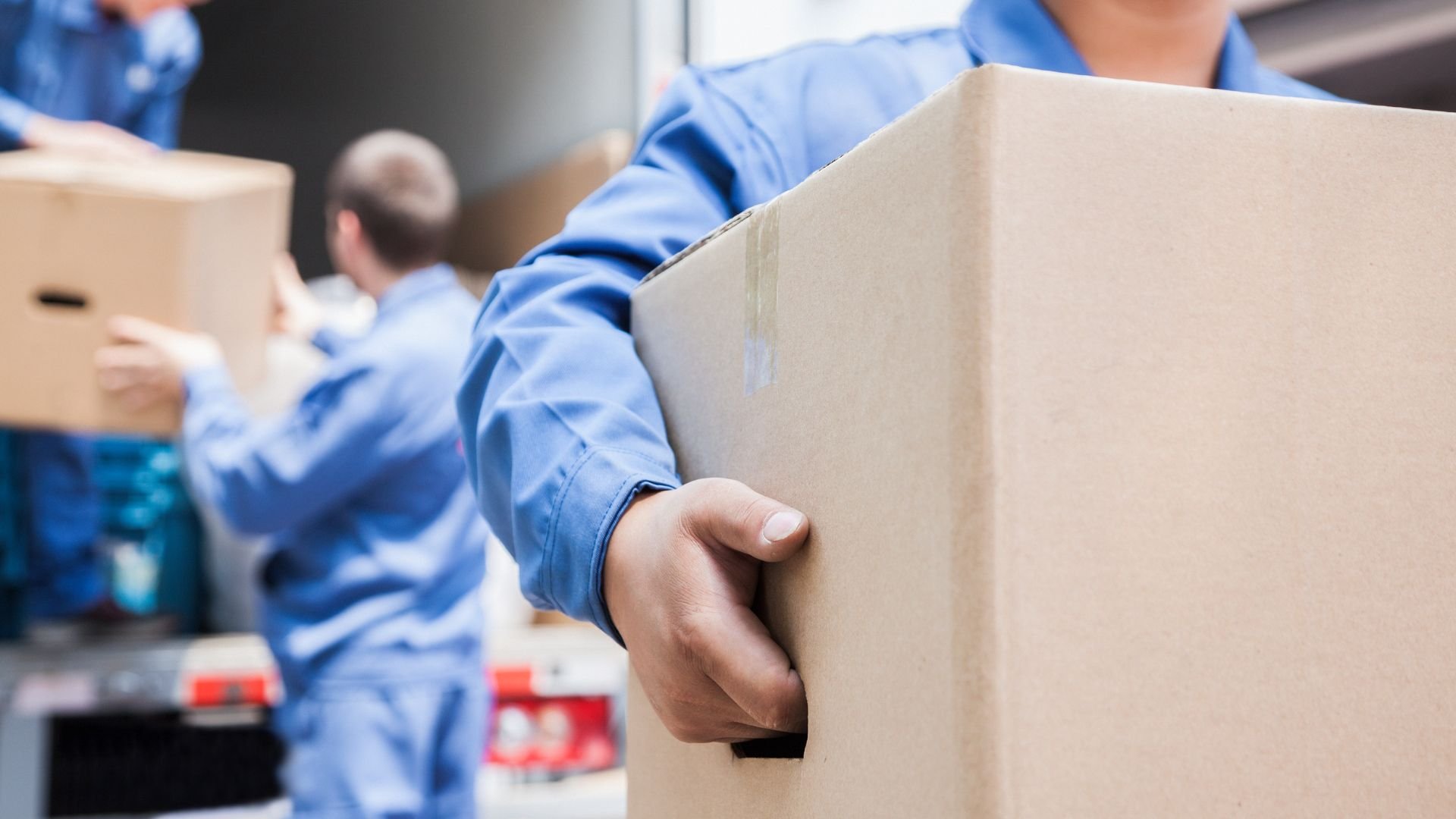 Movers in blue uniforms carrying cardboard boxes during relocation