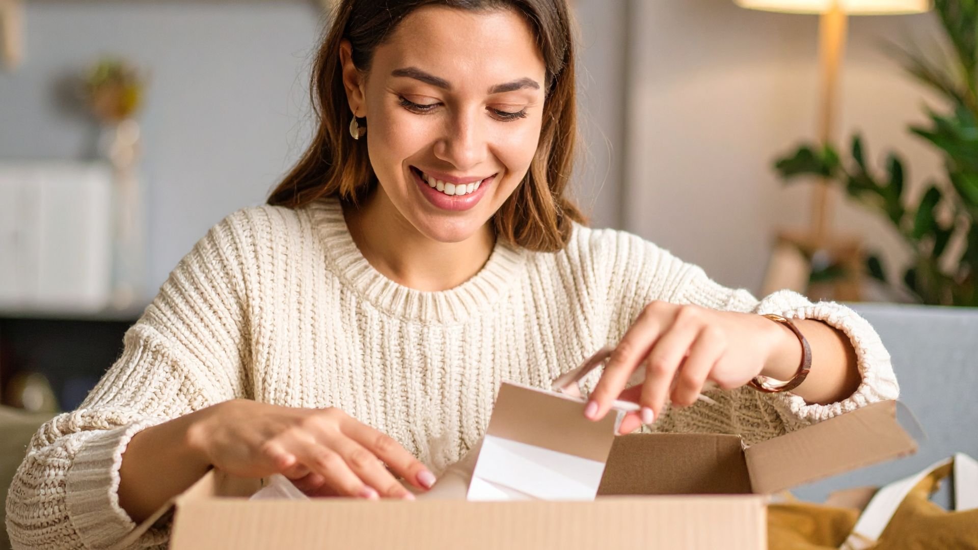 Smiling woman in white sweater opening package at home