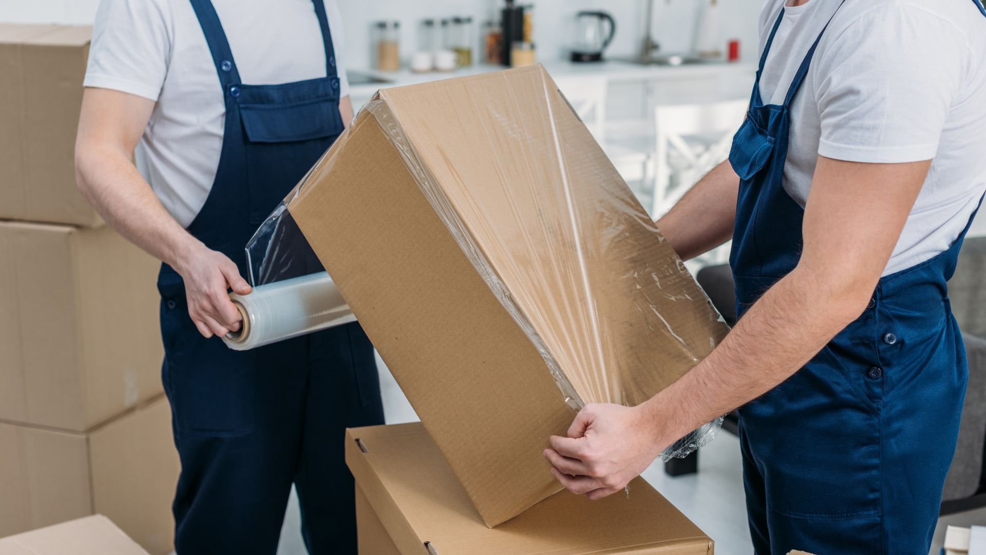 Movers in blue overalls wrapping and preparing cardboard boxes for transport