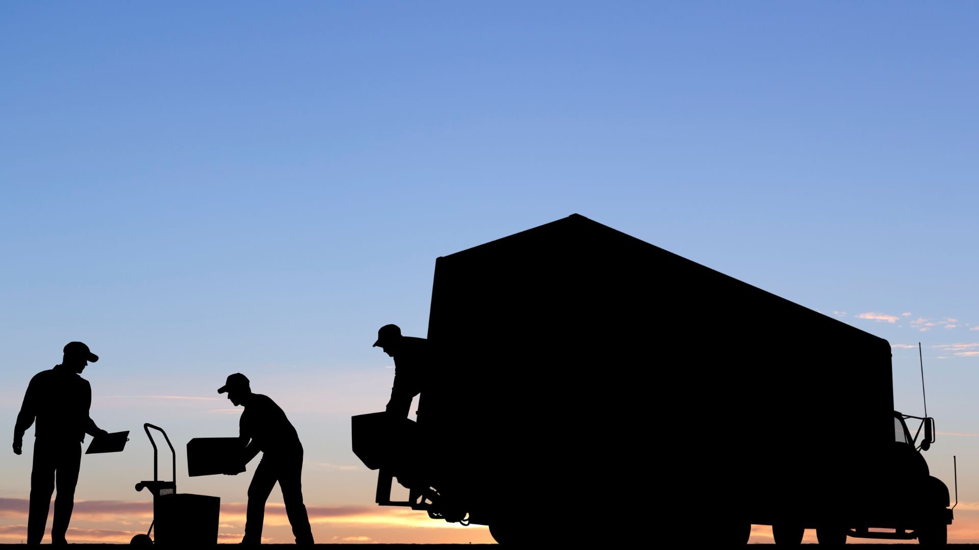 Silhouetted workers loading boxes into truck at sunrise or sunset