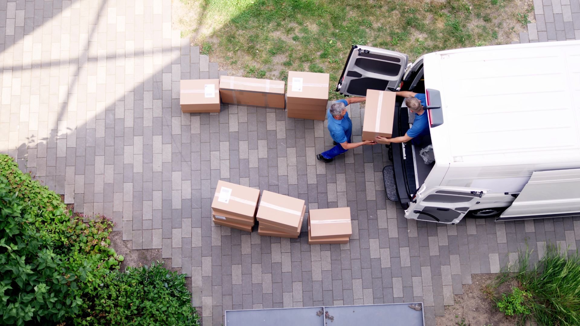 Delivery workers unloading cardboard boxes from a white van on a paved area