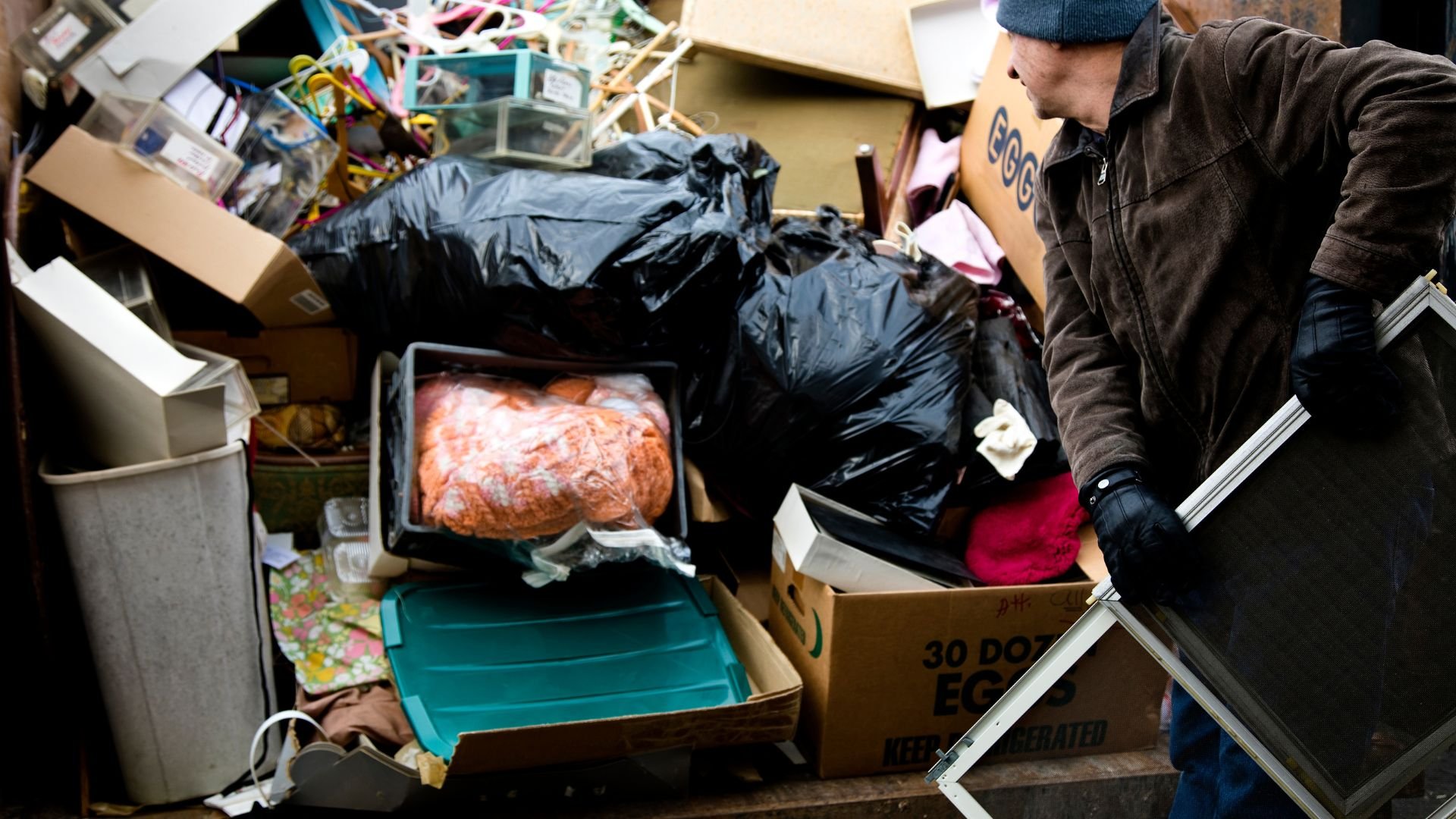 Cluttered storage area with trash bags, boxes, and person sorting items