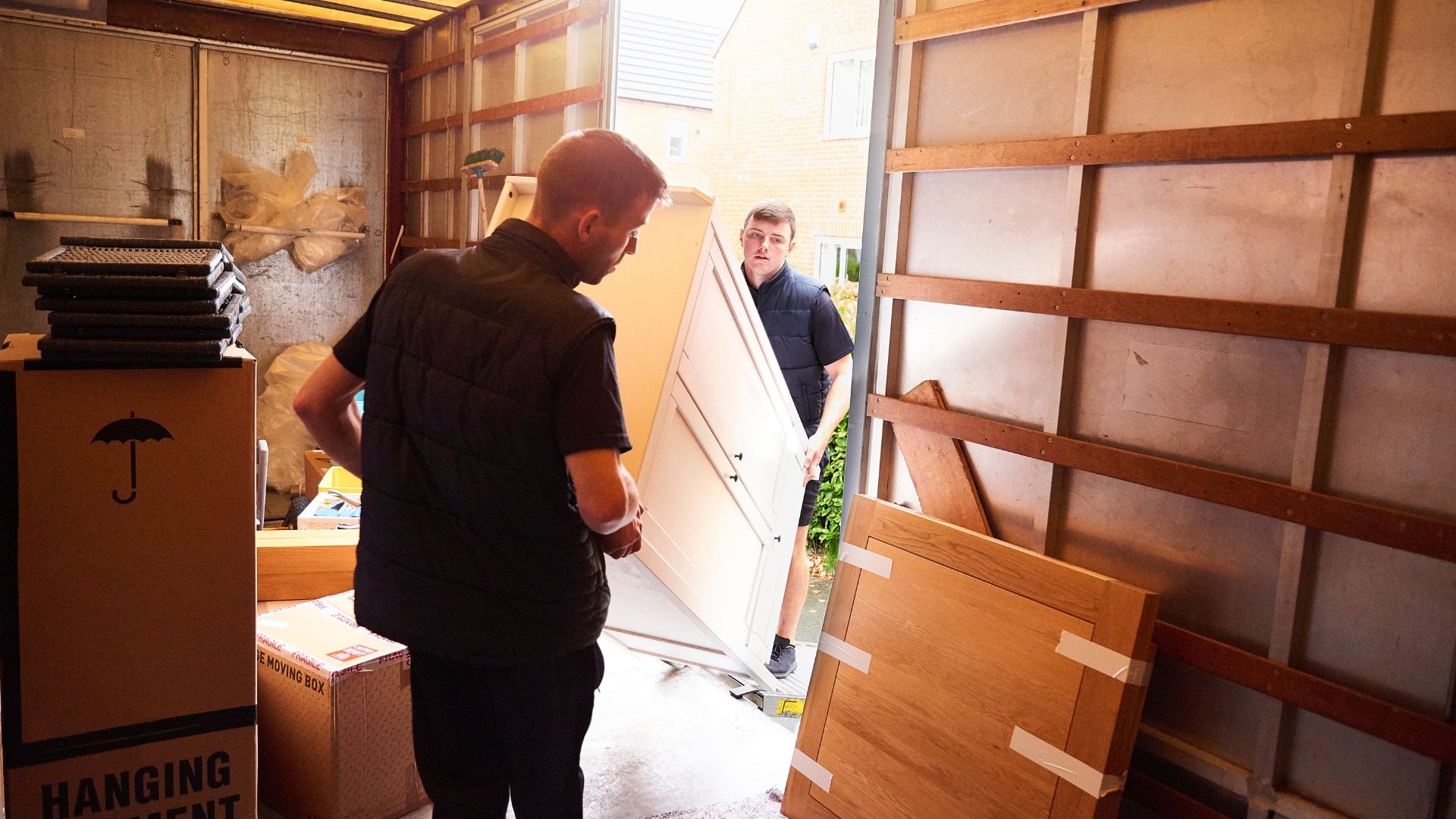 Two workers moving large wooden boards in a storage or workshop space