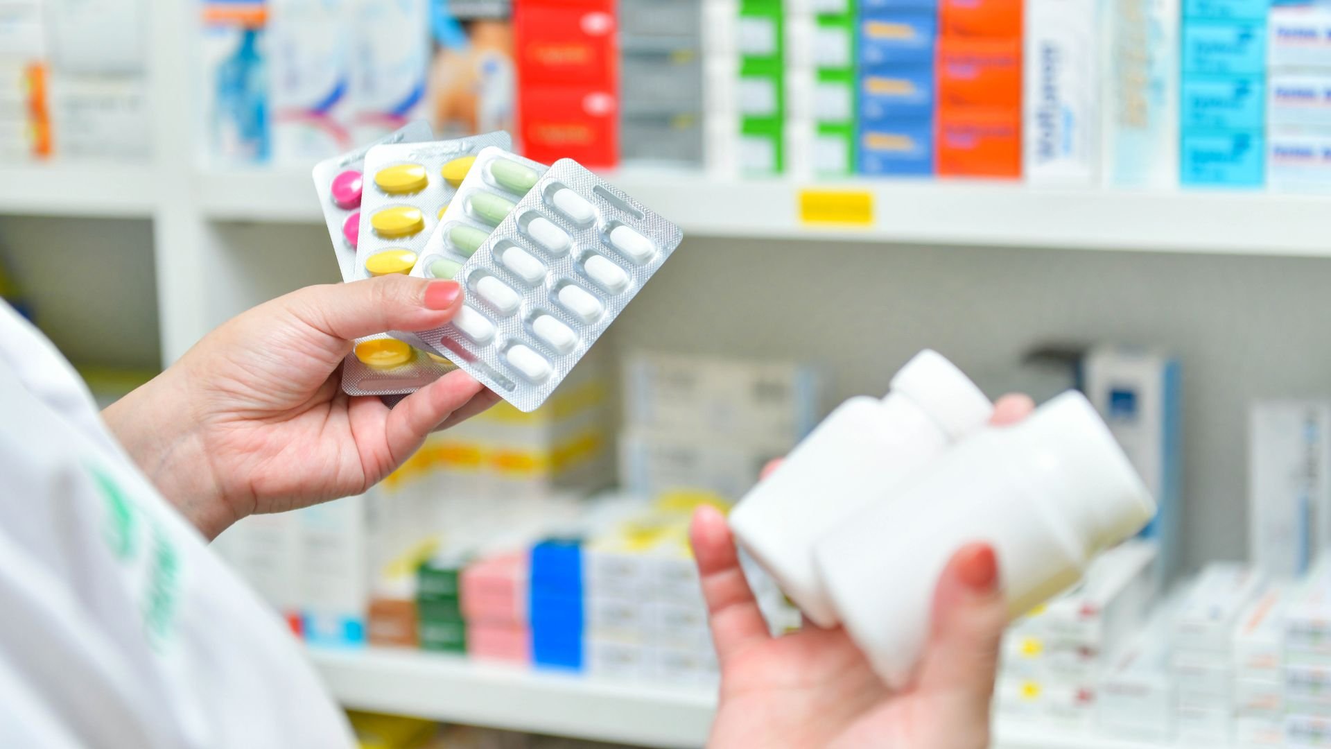 Pharmacist holding different colored medication blister packs in pharmacy