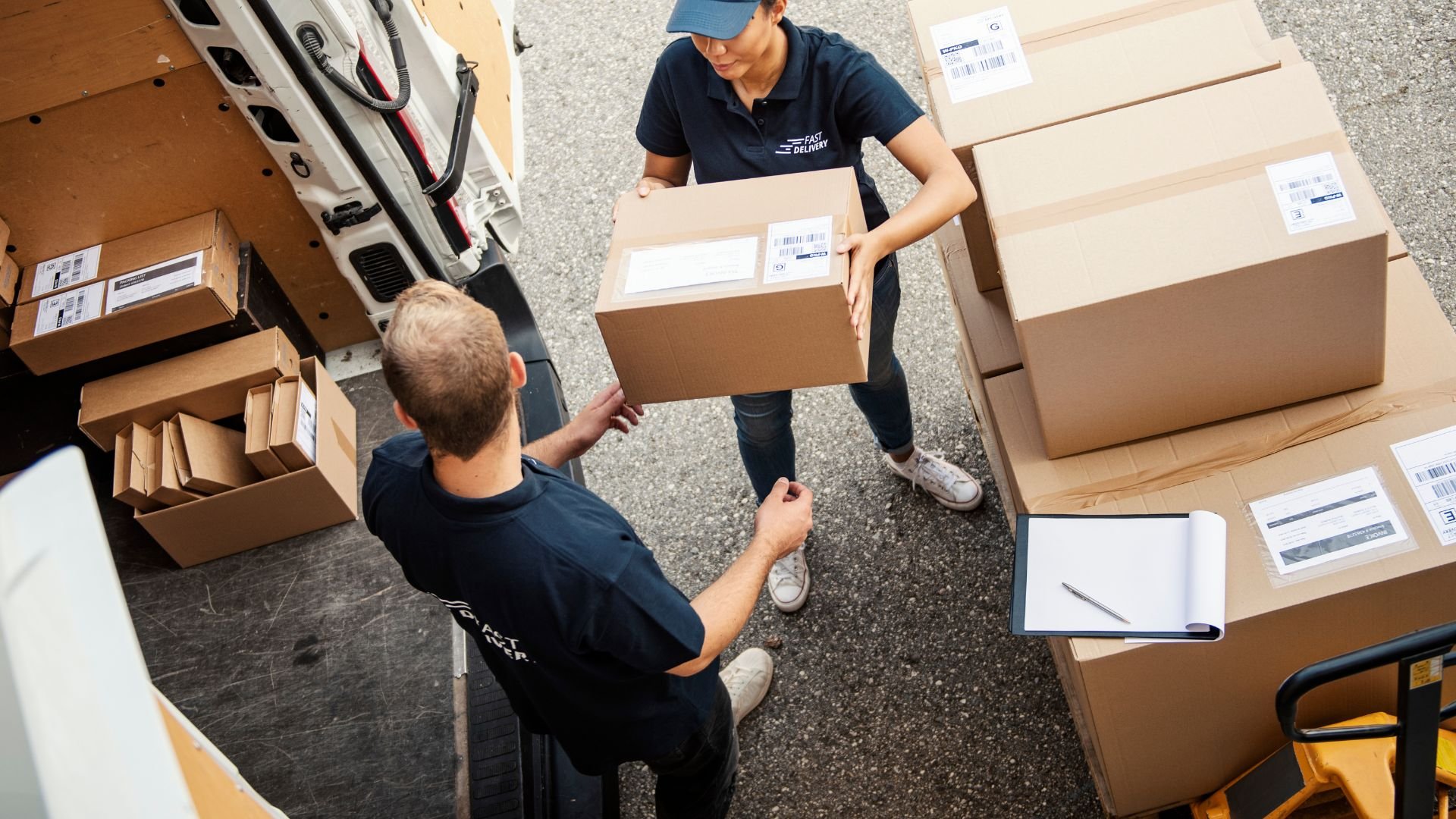 Delivery workers loading cardboard packages into a van near a clipboard